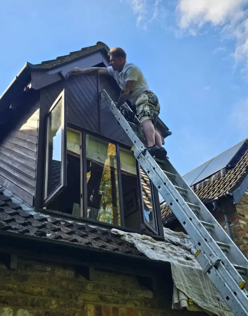 painters and decorators ruislip - exterior house painting - image shows Frazer up a ladder painting a house gable, he is wearing a white tshirt and black shorts