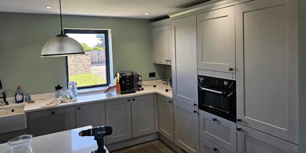 kitchen cabinet painting - grey cabinet doors, white worktops light green walls and window showing grass outside --- painting and decorating services, plasterers near me, plastering contractors, re grouting tiles, spacers in ruislip